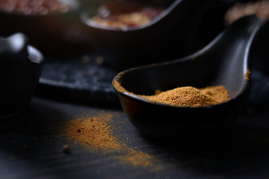 Spices and herbs on dark background, yellow turmeric powderin tablespoon with assorted colorful of seasoning ingredients as blurred background
