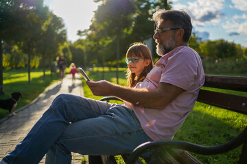 Grandfather and granddaughter taking selfie with mobile phone at park