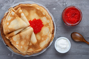 Stack of russian thin pancakes blini with red caviar and fresh sour cream