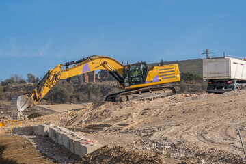 Large yellow excavator depositing sand and earth in a white truck bed at a large construction site