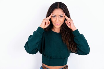 teen girl with curly hair wearing green sweater over white background concentrating hard on an idea with a serious look, thinking with both index fingers pointing to forehead.