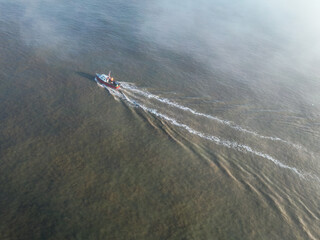 Naklejka premium Aerial view of a small pleasure fishing boat with sea anglers on board. A dense fog bank is starting the engulf the area and is causing a hazard to shipping.