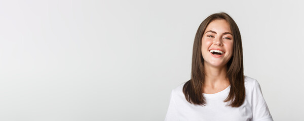 Close-up of happy brunette girl in white t-shirt laughing and smiling carefree at camera