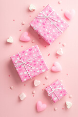 Valentine's Day concept. Top view vertical photo of gift boxes in wrapping paper with heart pattern candles marshmallow and sprinkles on isolated pastel pink background