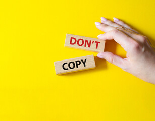 Don't copy symbol. Wooden blocks with words Don't copy. Beautiful yellow background. Businessman hand. Business and Don't copy concept. Copy space.