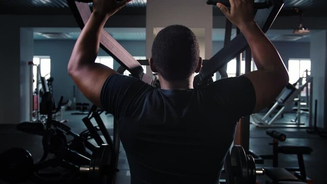 Black man training back muscle doing pulls weight exercise in a gym.Athlete do workout in simulator machine new equipment.Bodybuilder pumping back sitting on gym machine.