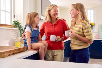 Same Sex Family With Two Mature Mums And Daughter Sitting In Kitchen Talking Together