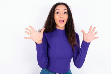 Delighted positive beautiful teen girl wearing knitted purple sweater over white background opens mouth  and arms palms up after having great result