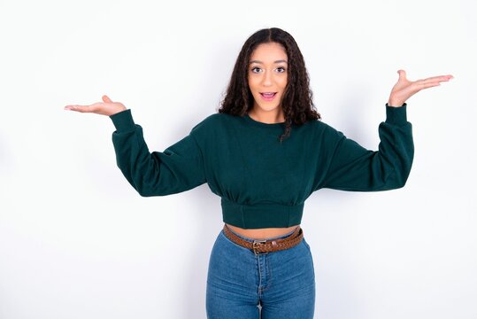 teen girl wearing knitted green sweater over white background raising hands up, having eyes full of happiness rejoicing his great achievements. Achievement, success concept.