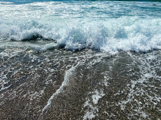 Waves of water in the sea and sand with small natural multi-colored stones on the seashore, small pebbles on the beach. Background, texture