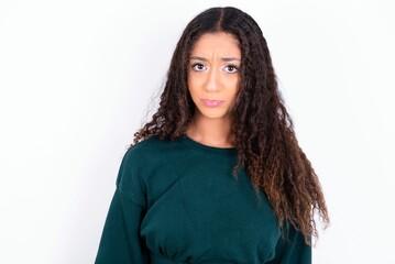 teen girl wearing knitted green sweater over white background crying desperate and depressed with tears on his eyes suffering pain and depression. Sad facial expression and emotion concept.