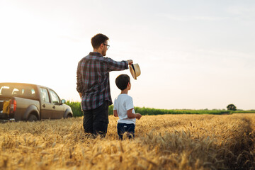 Father and son are standing in their growing wheat field and enjoying it together
