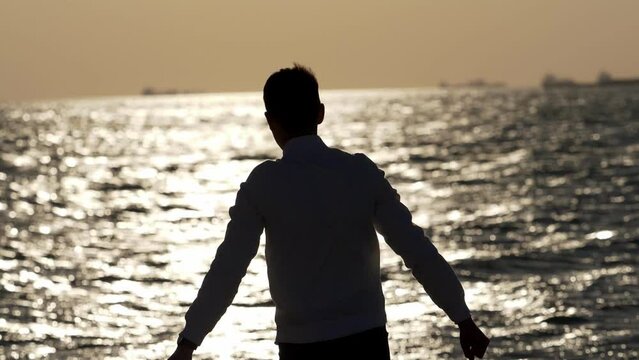 guy by the sea at sunset rejoicing after throwing a stone into the water 