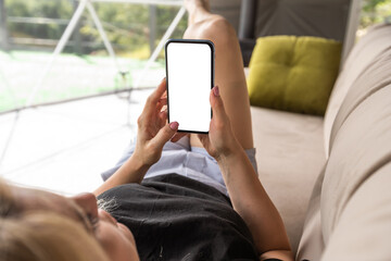 Happy young caucasian woman relax on comfortable couch at home texting messaging on smartphone, use cellphone, browse wireless internet on gadget, shopping online from home