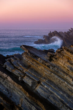 Pink glowing sunset sky over the Atlantic Ocean and the rugged rocks lining the coastline at Praia Baleal; Peniche, Oeste, Portugal