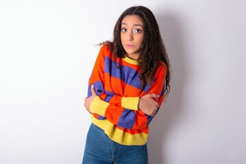 beautiful teen girl wearing knitted colourful sweater over white background shaking and freezing for winter cold with sad and shock expression on face.