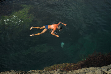 A man in a diving mask swims in the clear water of the lagoon among the rocks near a large jellyfish