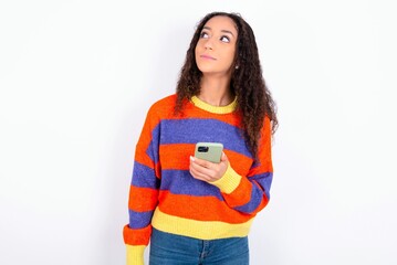 beautiful teen girl wearing knitted colourful sweater over white background holds mobile phone uses high speed internet and social networks has online communication. Modern technologies concept