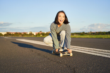 Portrait of carefree, happy asian girl skating, riding skateboard and laughing, enjoying sunny day