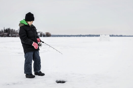 Boy patiently waiting for a bite while ice fishing at Wabamun Lake; Wabamun, Alberta, Canada