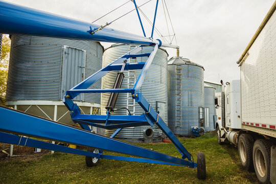 An auger assembly and grain truck parked beside silos in a farmyard; Legal, Alberta, Canada