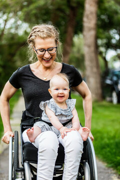A paraplegic mom carrying her baby in her lap while using a wheelchair outdoors on a warm summer afternoon: Edmonton, Alberta, Canada