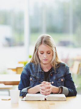 A mature woman praying, after doing some personal Bible study, in a coffee shop : Edmonton, Alberta, Canada