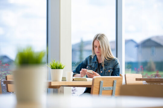 A mature Christian woman studying her bible in a coffee shop and doing some extra research on her smart phone: Edmonton, Alberta, Canada