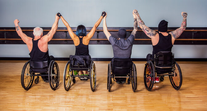A view from behind of a group of paraplegic friends holding their hands high in a victory celebration after a workout in fitness facility: Sherwood Park, Alberta, Canada