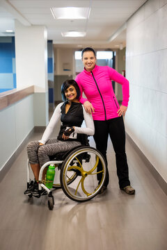 A paraplegic woman and her trainer pose for the camera while in a hallway in a recreational facility: Sherwood Park, Alberta, Canada