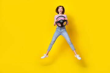 Fototapeta na wymiar Full length photo of nice cute adorable girl with bob hairstyle wear striped shirt jeans flying hold steering wheel isolated on yellow color background