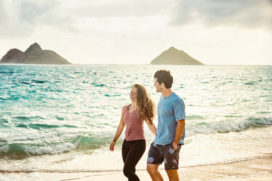 A young Millennial couple walking along Lanikai Beach with the Mokes Islands in the background; Lanikai, Oahu, Hawaii, USA