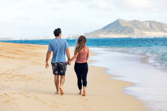 A view from behind of a Millennial couple walking along Lanikai Beach with Mokapu Point in the background; Lanikai, Oahu, Hawaii, USA
