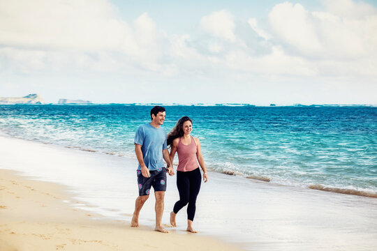 A Millennial couple walking along Lanikai Beach with Mokapu Point and the Moku Manu Islands in the background; Lanikai, Oahu, Hawaii, USA