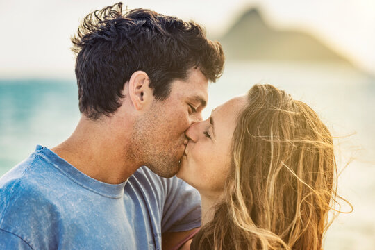 Millennial couple kissing on Lanikai Beach with the Mokes Islands in the background; Lanikai, Oahu, Hawaii, USA