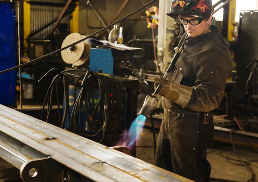Tradesman pre-heating steel beam with a lift lug using a torch; Innisfail, Alberta, Canada