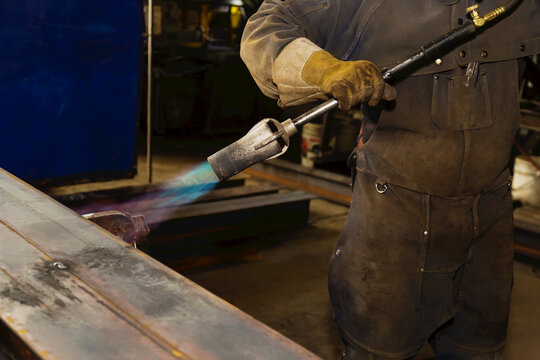 Tradesman pre-heating steel beam with a lift lug using a torch; Innisfail, Alberta, Canada