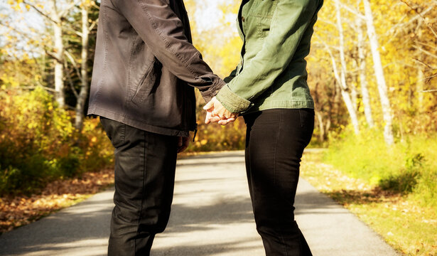 A mature married couple walking together and pausing to hold hands in a park during the fall season; St. Albert, Alberta, Canada