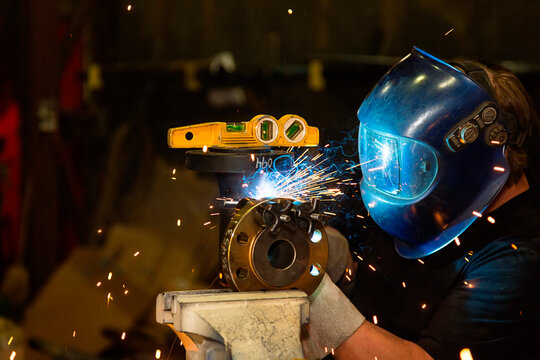 Sparks fly when a journeyman pipe fitter uses tack welding to attach a flange to fitting with a level in a metal fabrication plant; Innisfail, Alberta, Canada