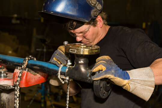 Pipe fitter inspects tack welds with a flashlight before butt welding a flange to a pipe in a metal fabrication plant; Innisfail, Alberta, Canada
