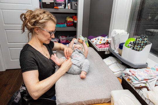 A mother in a wheelchair changes her baby's diaper on a changing table in a nursery; Edmonton, Alberta, Canada