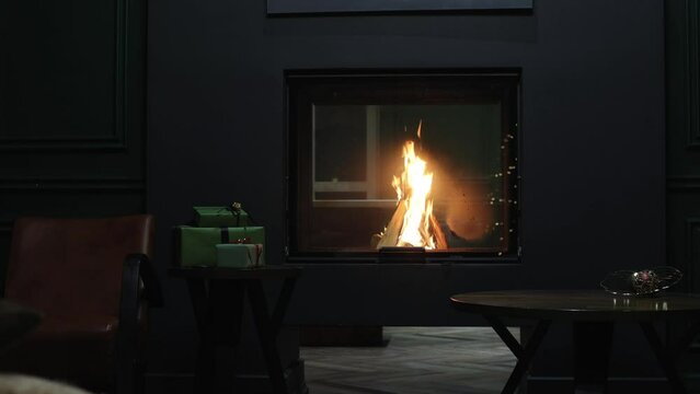 Empty room, burning fireplace. Christmas present, room interior celebration concept. Christmas tree branch with colorful balls, two gift boxes with golden ribbons, burning fireplace background. Warm f