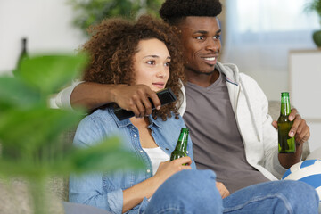 young mixed-race couple having a beer while watching tv
