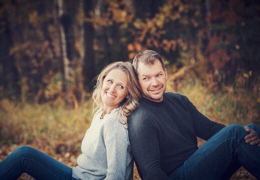 A married couple sitting back to back while spending quality time together outdoors in a city park during a warm fall afternoon; St. Albert, Alberta, Canada