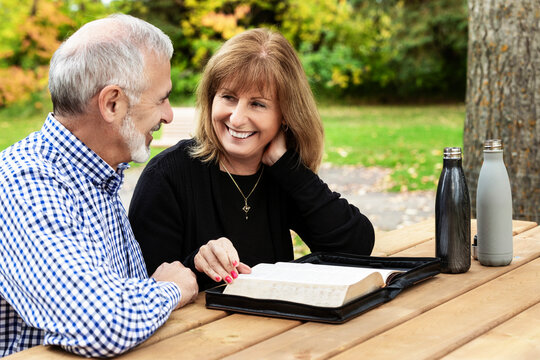 A mature couple sharing devotional time together and studying the bible at a picnic table on a warm fall day in a city park; St. Albert, Alberta, Canada