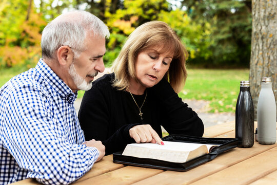 A mature couple sharing devotional time together and studying the bible at a picnic table on a warm fall day in a city park; St. Albert, Alberta, Canada