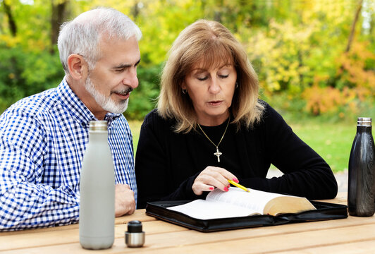A mature couple sharing devotional time together and studying the bible at a picnic table on a warm fall day in a city park; St. Albert, Alberta, Canada
