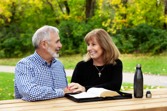 A mature couple sharing devotional time together and studying the bible at a picnic table on a warm fall day in a city park; St. Albert, Alberta, Canada