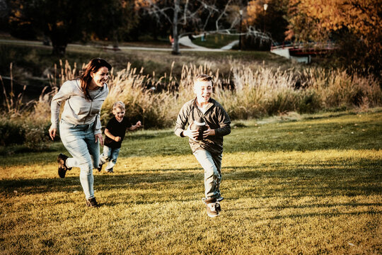 Mother chasing her son in a game of football on a beautiful autumn day in a city park; St. Alberta, Alberta, Canada