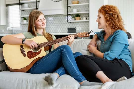 Mother and teen daughter spending quality time together at home while daughter plays guitar; Edmonton, Alberta, Canada